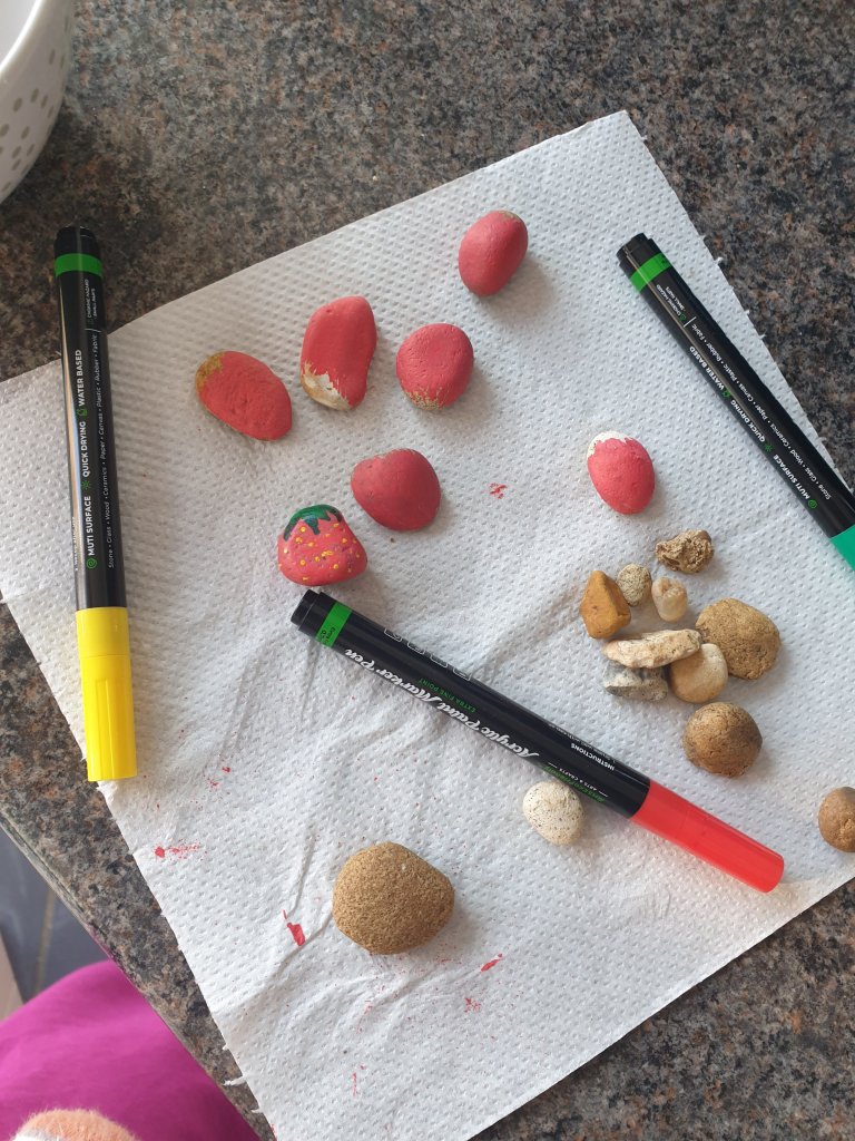 Small rocks on a counter. Some painted red and others not. Slowly they start to look like strawberries.